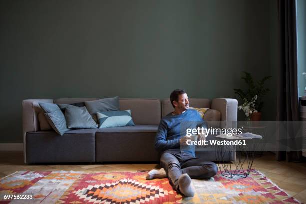 man sitting on the floor in his living room looking through window - man sitting on sofa fotografías e imágenes de stock