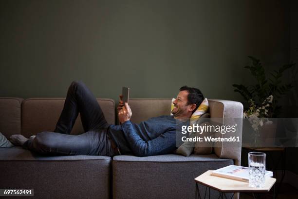 laughing man using tablet on couch at home - man couch foto e immagini stock