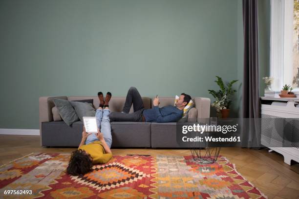 couple relaxing together in the living room with different electronic devices - man living room stockfoto's en -beelden