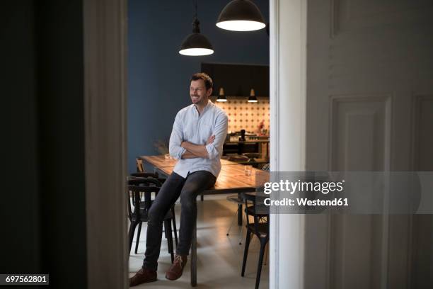 smiling man sitting on table in his kitchen - tisch betrachten stock-fotos und bilder