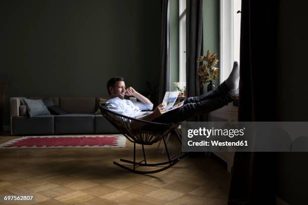 man relaxing on rocking chair in his living room reading newspaper - feet on table stock pictures, royalty-free photos & images