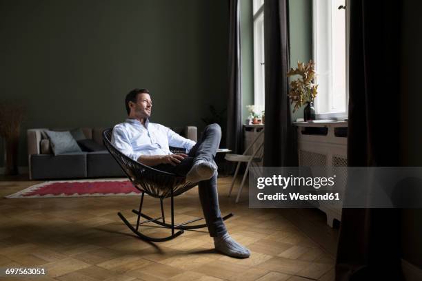 man sitting on rocking chair in his living room looking through window - schaukelstuhl stock-fotos und bilder