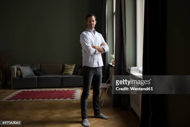 portrait of smiling man standing near window in his living room - mann stolz stock-fotos und bilder