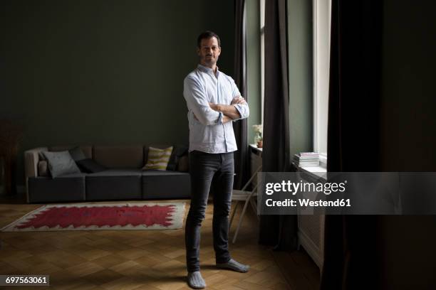 portrait of smiling man standing near window in his living room - vertical photos et images de collection