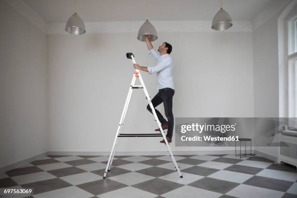 man standing on ladder in an empty room changing bulb of ceiling light - step ladder stock-fotos und bilder