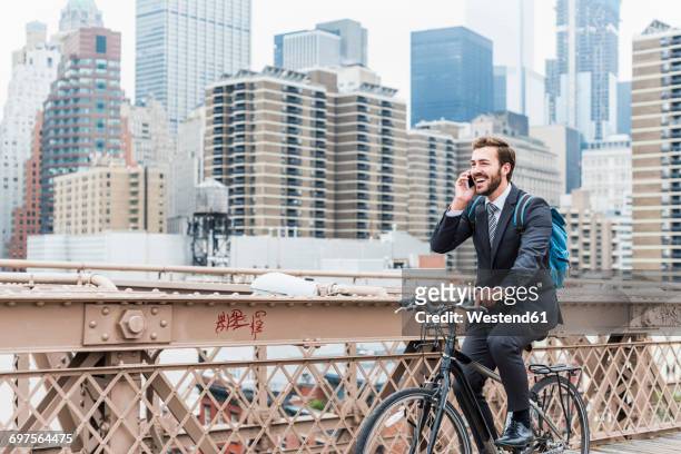 usa, new york city, laughing businessman on bicycle on brooklyn bridge using cell phone - ragazzo new york foto e immagini stock