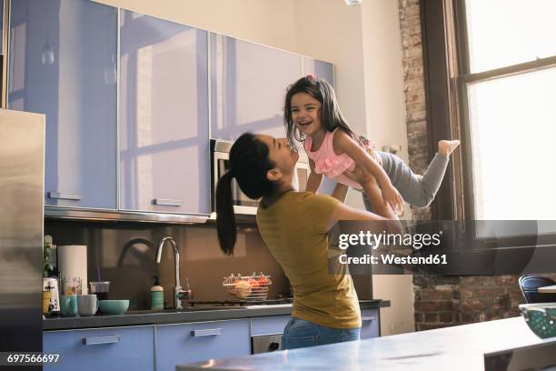 mother lifting daughter in kitchen - mother daughter hispanic stock pictures, royalty-free photos & images