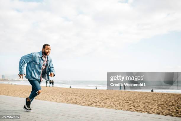 young man running on beach promenade - man in denim jacket stock pictures, royalty-free photos & images