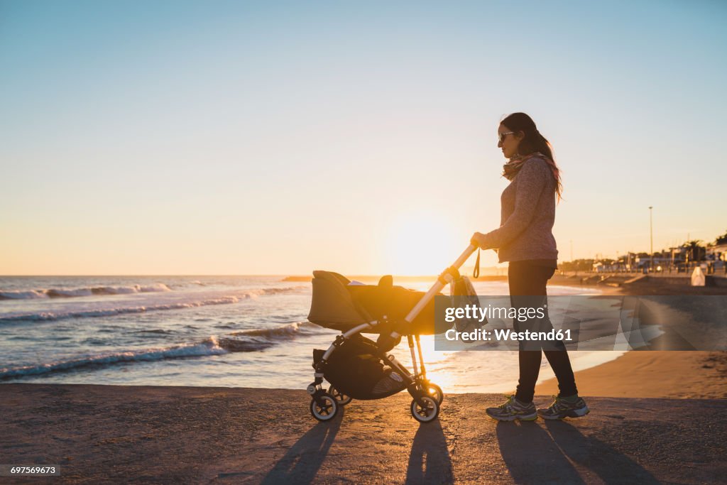 Woman walking with a stroller on the seashore at sunset