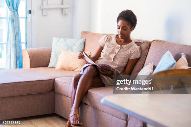 young woman sitting on the couch reading magazine - mujer revista fotografías e imágenes de stock