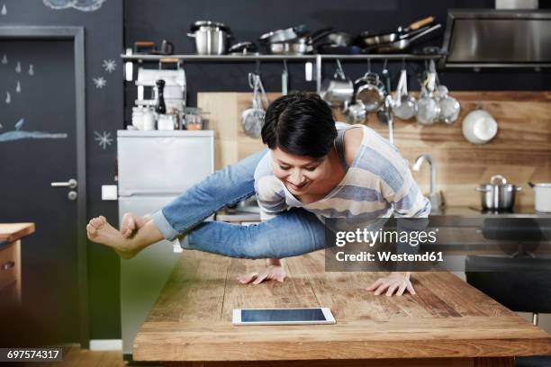 woman doing a handstand on table in kitchen looking on tablet - moeiteloos stockfoto's en -beelden