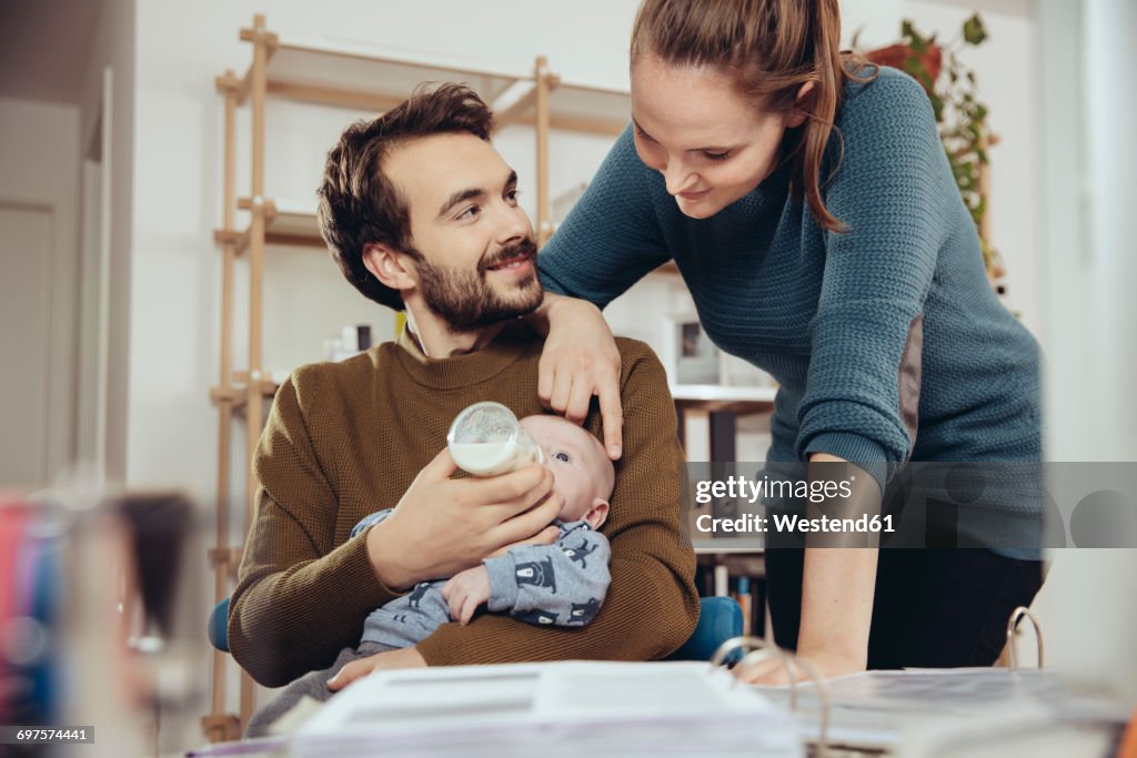 Mother looking at father feeding baby in home office