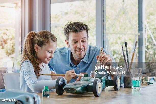 Father and daughter painting a toy race car