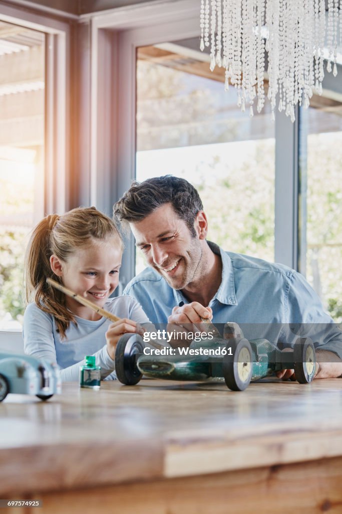 Father and daughter painting a toy race car