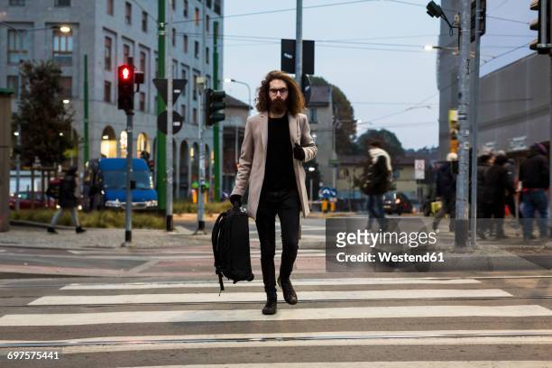 stylish young man with bag crossing street on zebra crossing - zebrastreifen stock-fotos und bilder