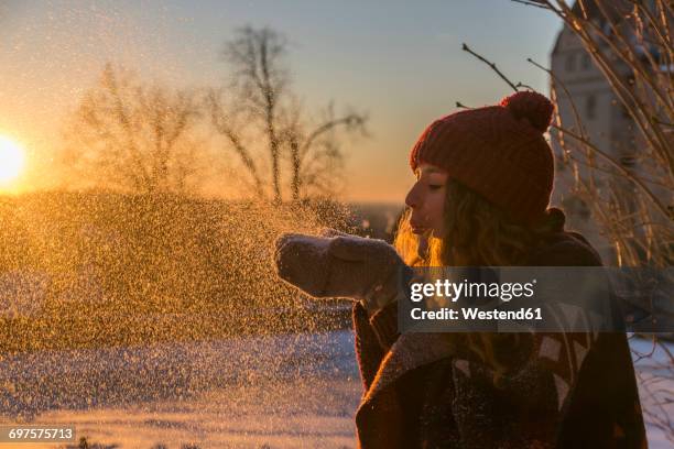 young woman blowing snow at sunset - bobble hat photos et images de collection