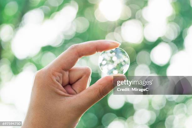 hand holding magnifying glass against green trees bokeh - magnifying glass nature stock-fotos und bilder