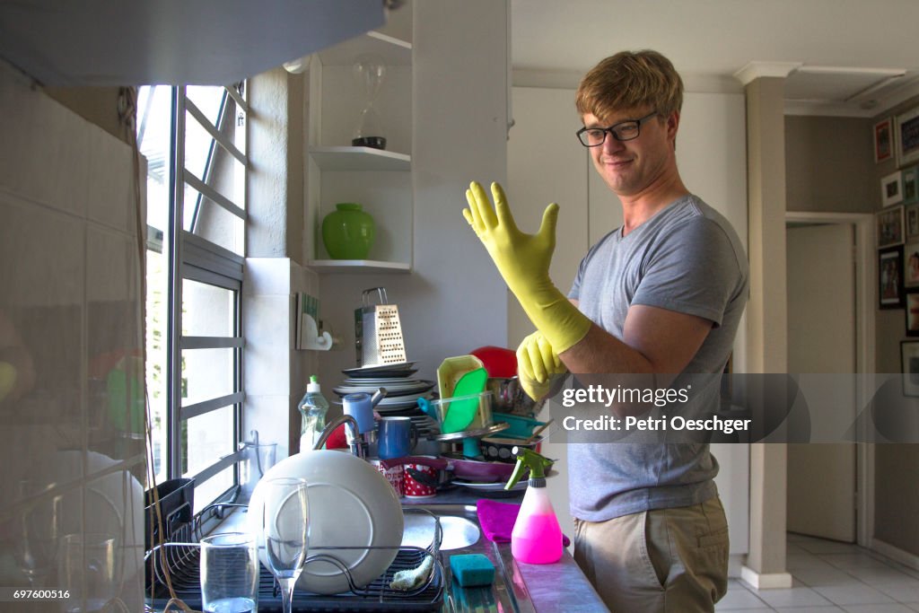 A Young man washing a large amount of dishes.
