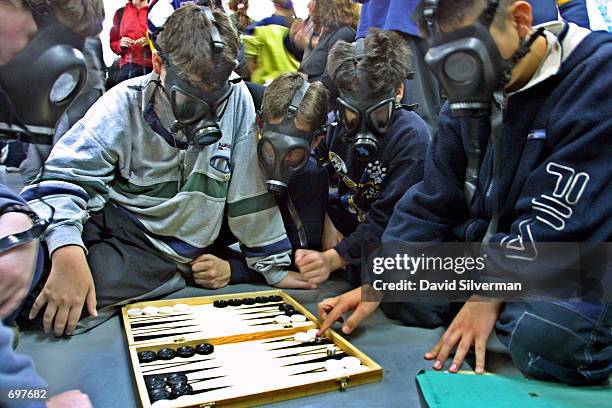 Israeli schoolboys wear gas masks while playing backgammon in a bomb shelter during a civil defense exercise at a school February 14, 2002 in the...