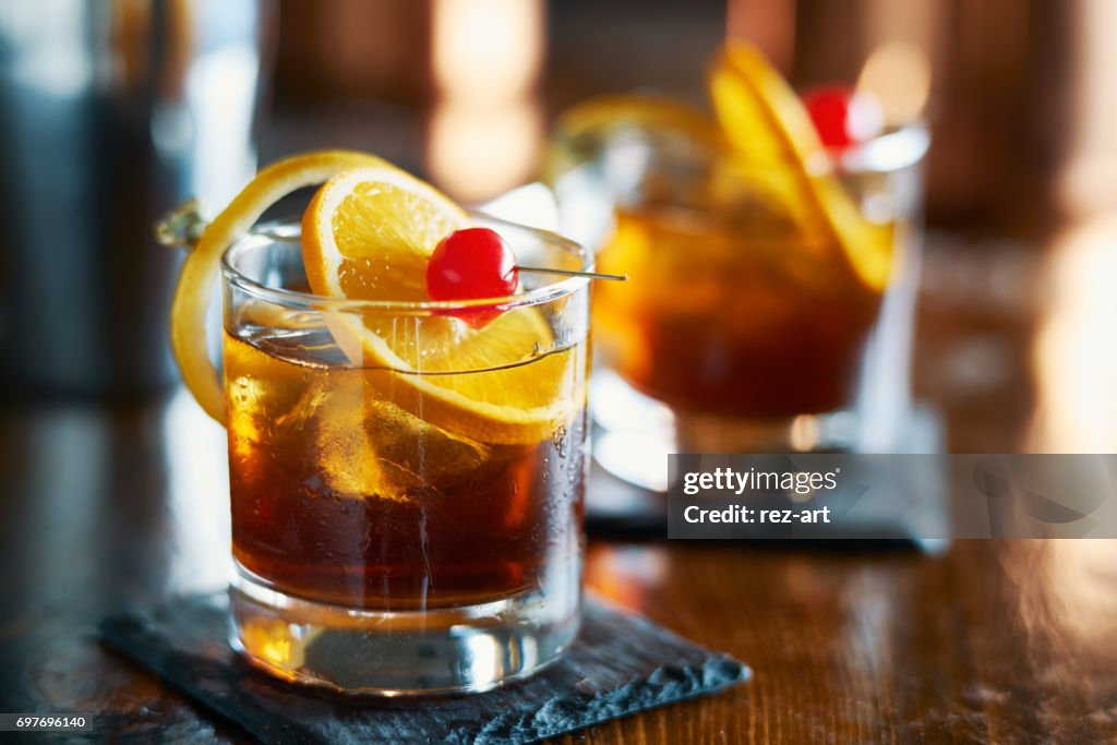 Tasty alcoholic old fashioned cocktail with orange slice, cherry, and lemon peel garnish