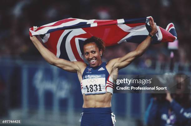 English track athlete Kelly Holmes raises her arms in the air to hold a union jack flag in celebration after crossing the finish line in third place...