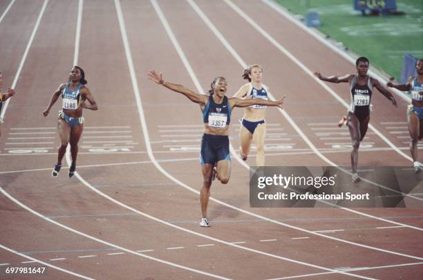 American track athlete Marion Jones raises her arms in the air in celebration after crossing the finish line in first place to win the gold medal for...