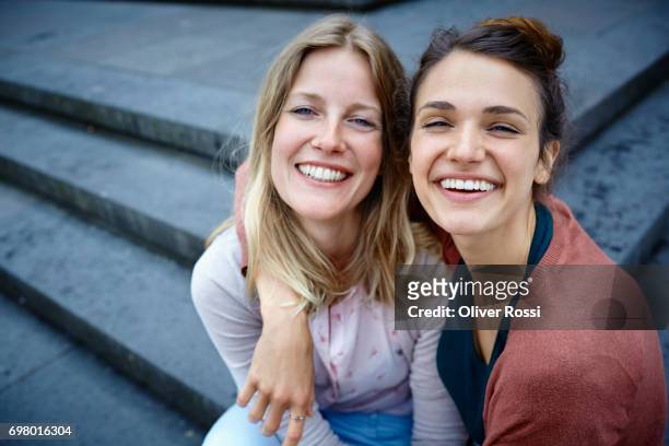 portrait of two happy women embracing on stairs - female friendship stock pictures, royalty-free photos & images