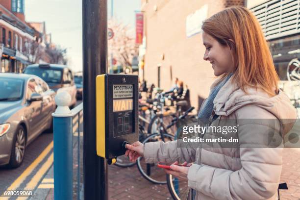 smiling woman pressing the stoplight button at the pedestrian walkway - sinal de peão imagens e fotografias de stock