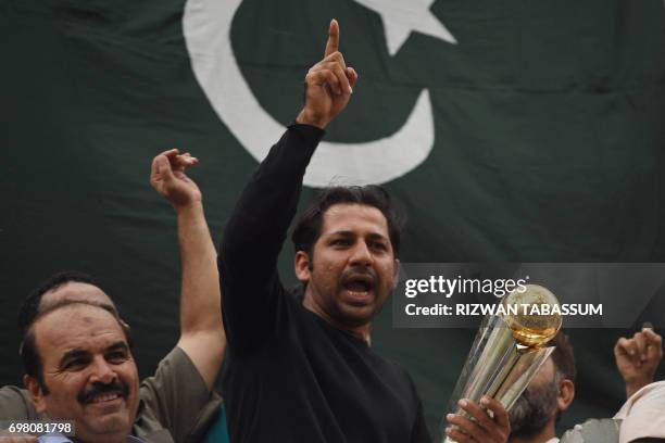 Pakistani cricket captain Sarfaraz Ahmed acknowledges fans as he holds the Champions Trophy following his arrival from London in Karachi on June 20...