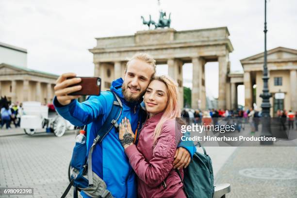 young couple stop to take selfie in front of brandenburg gate in berlin - rosa germanica foto e immagini stock