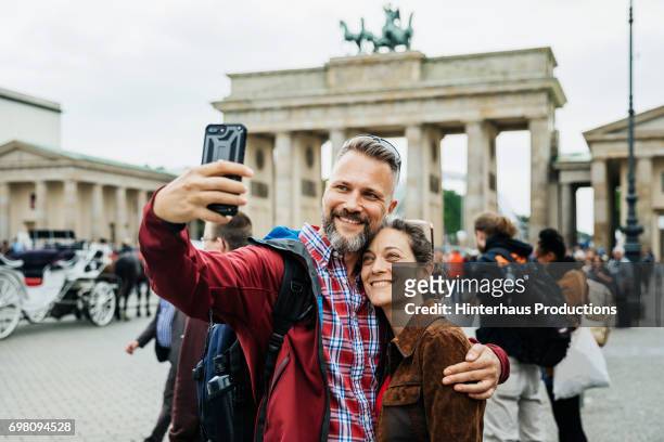 a mature couple take a selfie together in front of brandenburg gate in berlin - couple traveling stock pictures, royalty-free photos & images