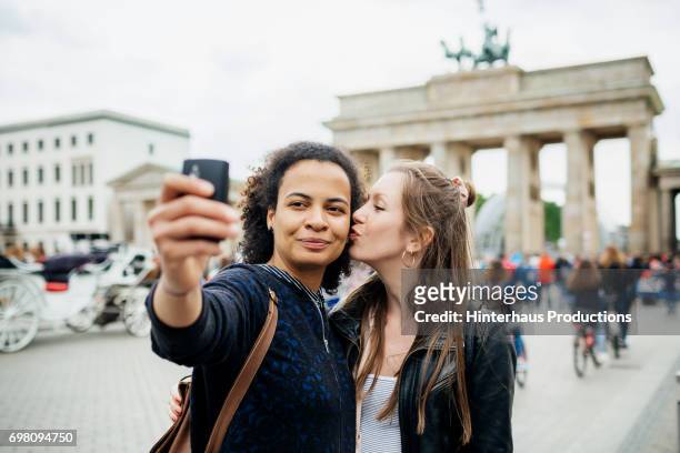 young lesbian couple stop to take a selfie at brandenburg gate in berlin - lesbische stock-fotos und bilder