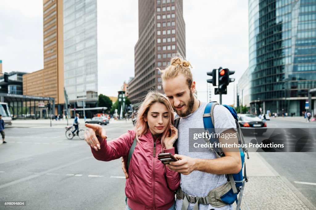 A Young Backpacking Couple Standing On Corner Of Busy City Street
