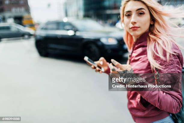 young woman moving through a city holding smartphone - in den zwanzigern stock-fotos und bilder