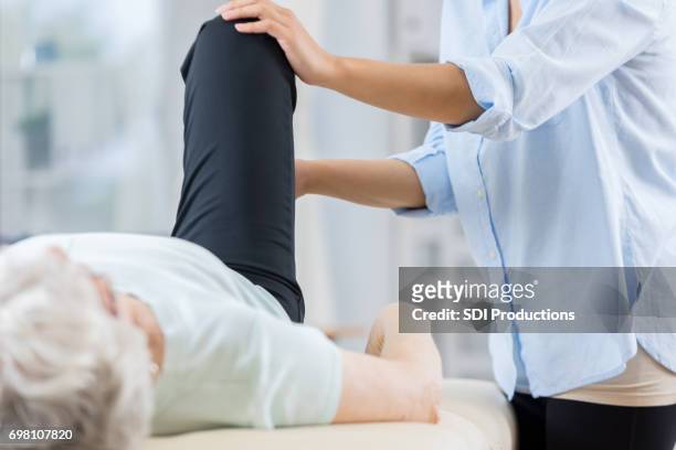 senior woman and therapist work on her knee - standing with hands on knees imagens e fotografias de stock