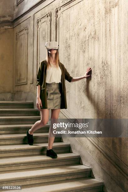 woman or young girl feels her way down the stairs of a building while experiencing virtual reality via a headset sensing her way while dressed stylish - down blouse imagens e fotografias de stock