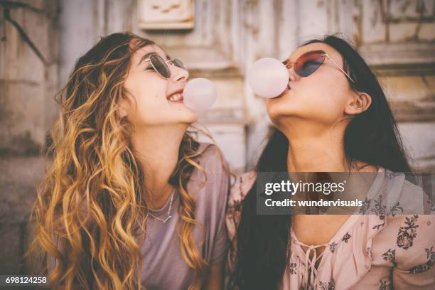 young women blowing bubbles with bubble gum in urban setting - bubble gum bubble stock pictures, royalty-free photos & images