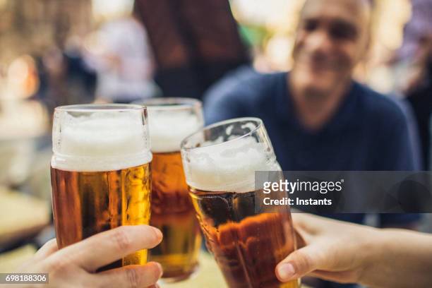 in prague, three friends cheering on good news with glasses of pilsner beer. - czech republic stock pictures, royalty-free photos & images