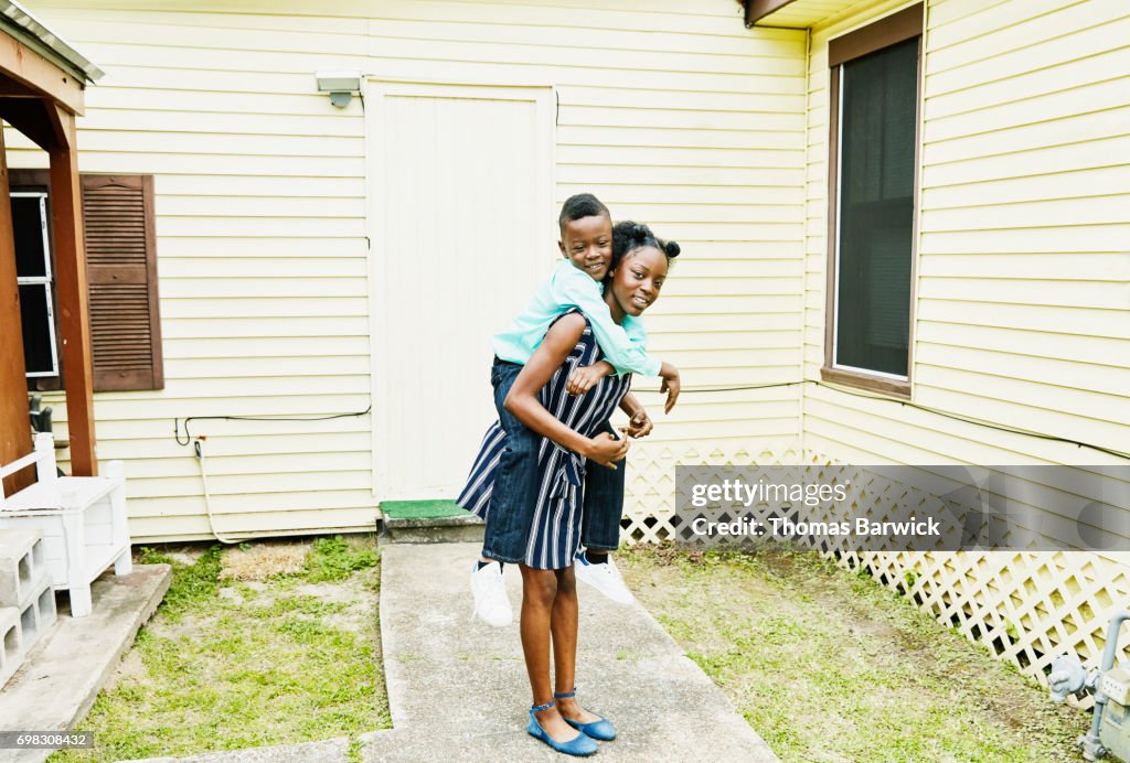 Smiling young woman carrying younger brother on back