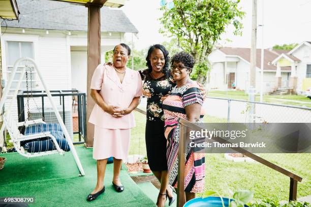 laughing mother and adult daughters standing on front porch of home before church - multi colored dress - fotografias e filmes do acervo