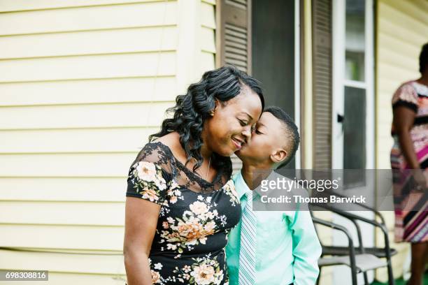 young boy kissing mother on cheek on front porch of home - black family reunion stock pictures, royalty-free photos & images