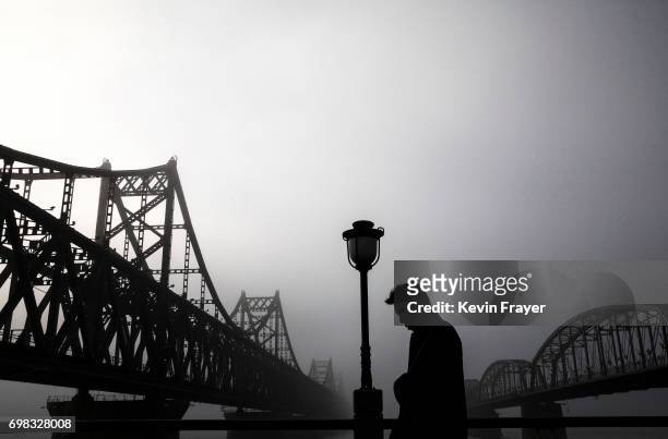 Chinese man walks in the rain between "Friendship Bridge", left, and "Broken Bridge", right, as he looks across the Yalu river from the border city...