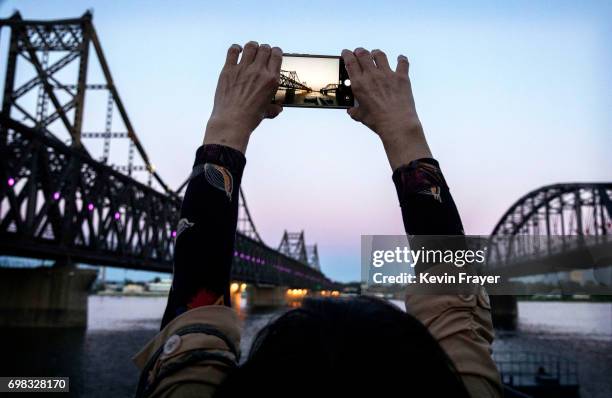 Chinese tourist takes pictures between "Friendship Bridge", left, and "Broken Bridge", right, as she looks across the Yalu river from the border city...