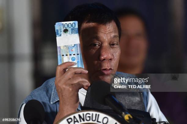 Philippines' President Rodrigo Duterte holds a wad of peso bills, which he later gave to evacuees from Marawi, while speaking to them in Iligan on...