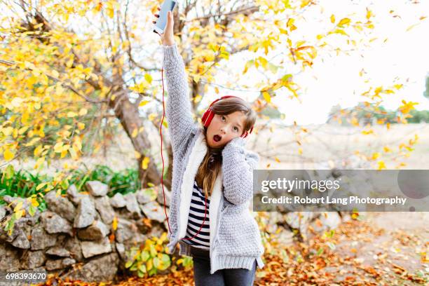 young girl listening to music through headphones while outside under a colourful pretty tree during the fall - under tongue 個照片及圖片檔