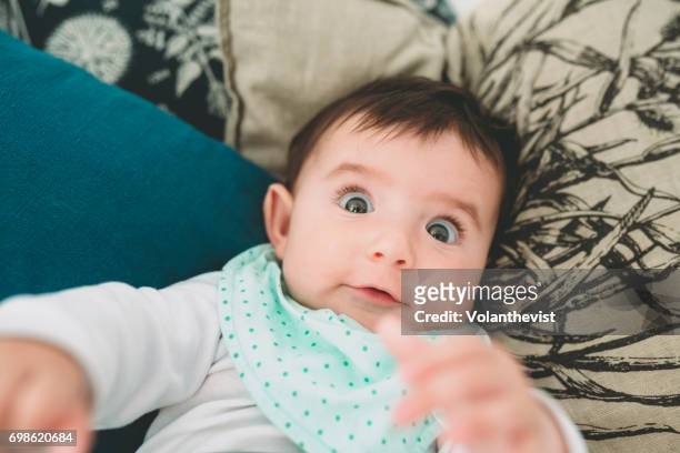 baby girl lying on the couch with surprised funny face - funny face baby stock pictures, royalty-free photos & images