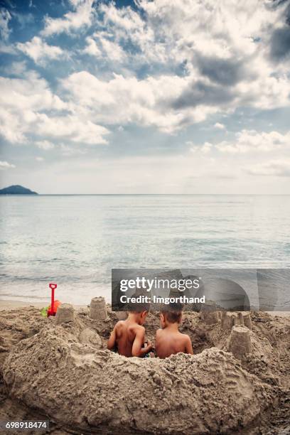 två små pojkar som sitter i ett sandslott på stranden - sand castle bildbanksfoton och bilder