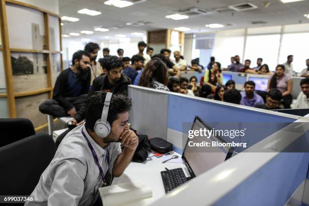 An employee uses headphones while working at a computer as his colleagues gather for a storyboard meeting at the Think and Learn Pvt. Office in...