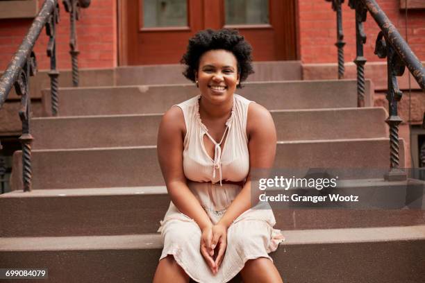 portrait of smiling black woman sitting on urban front stoop - portico sopraelevato foto e immagini stock