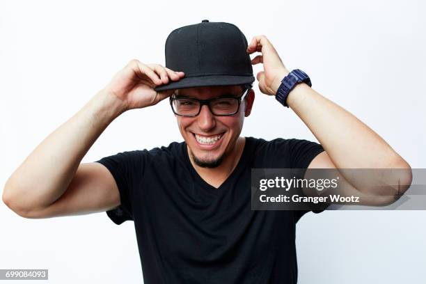 smiling hispanic man adjusting baseball cap - cap hat stockfoto's en -beelden